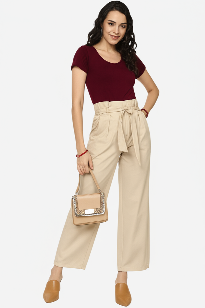Woman wearing a burgundy top and beige pants with a beige handbag on a white background