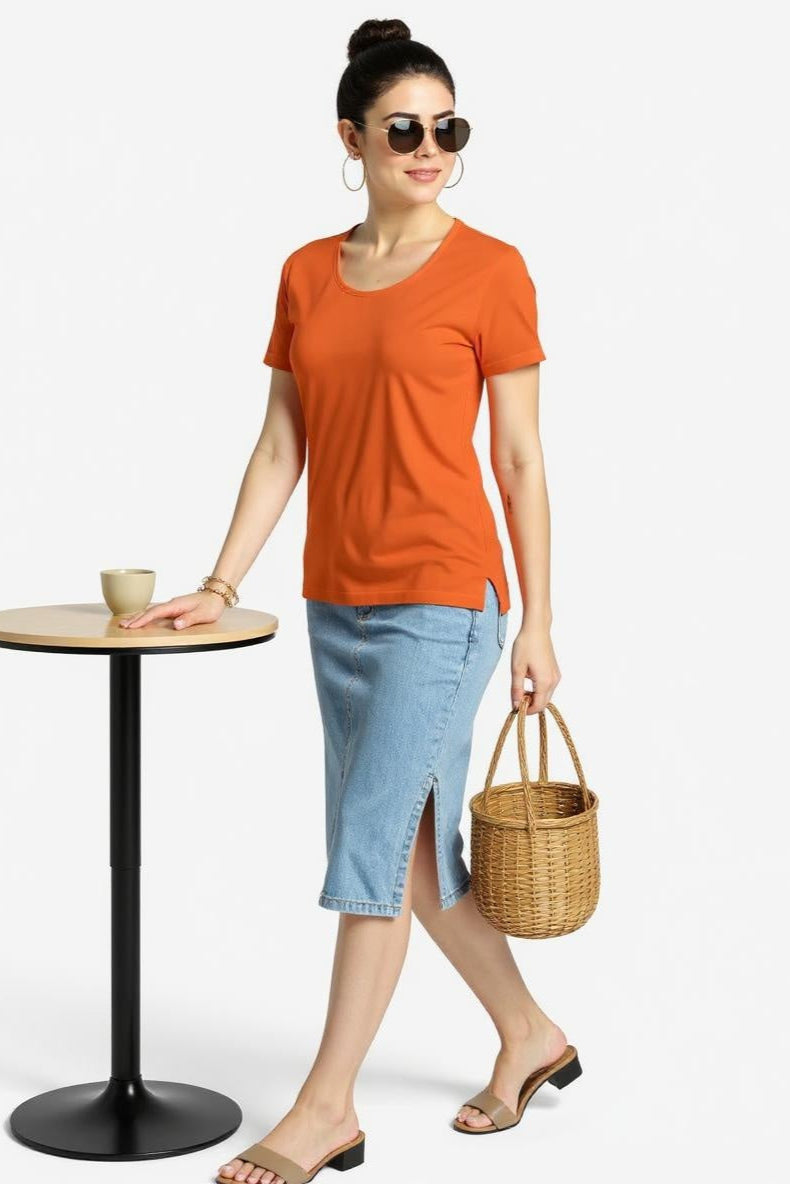 Woman in orange shirt and denim skirt holding a basket, standing next to a small table.
