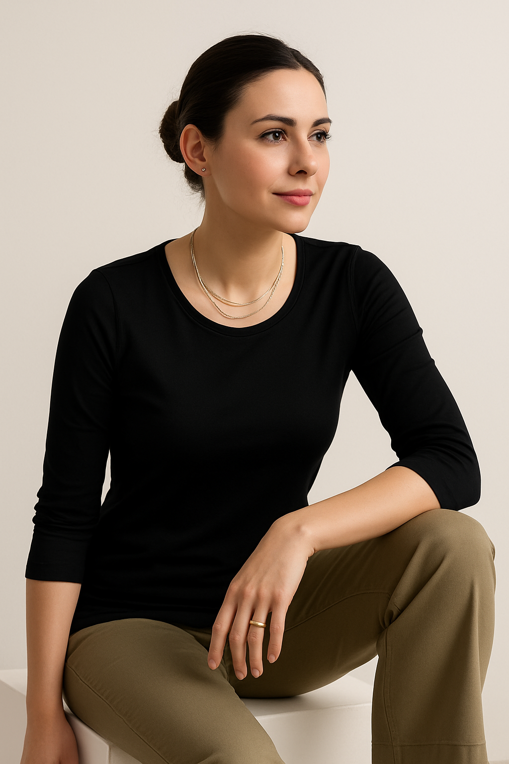Woman wearing a black top and brown pants sitting on a white surface with a beige background