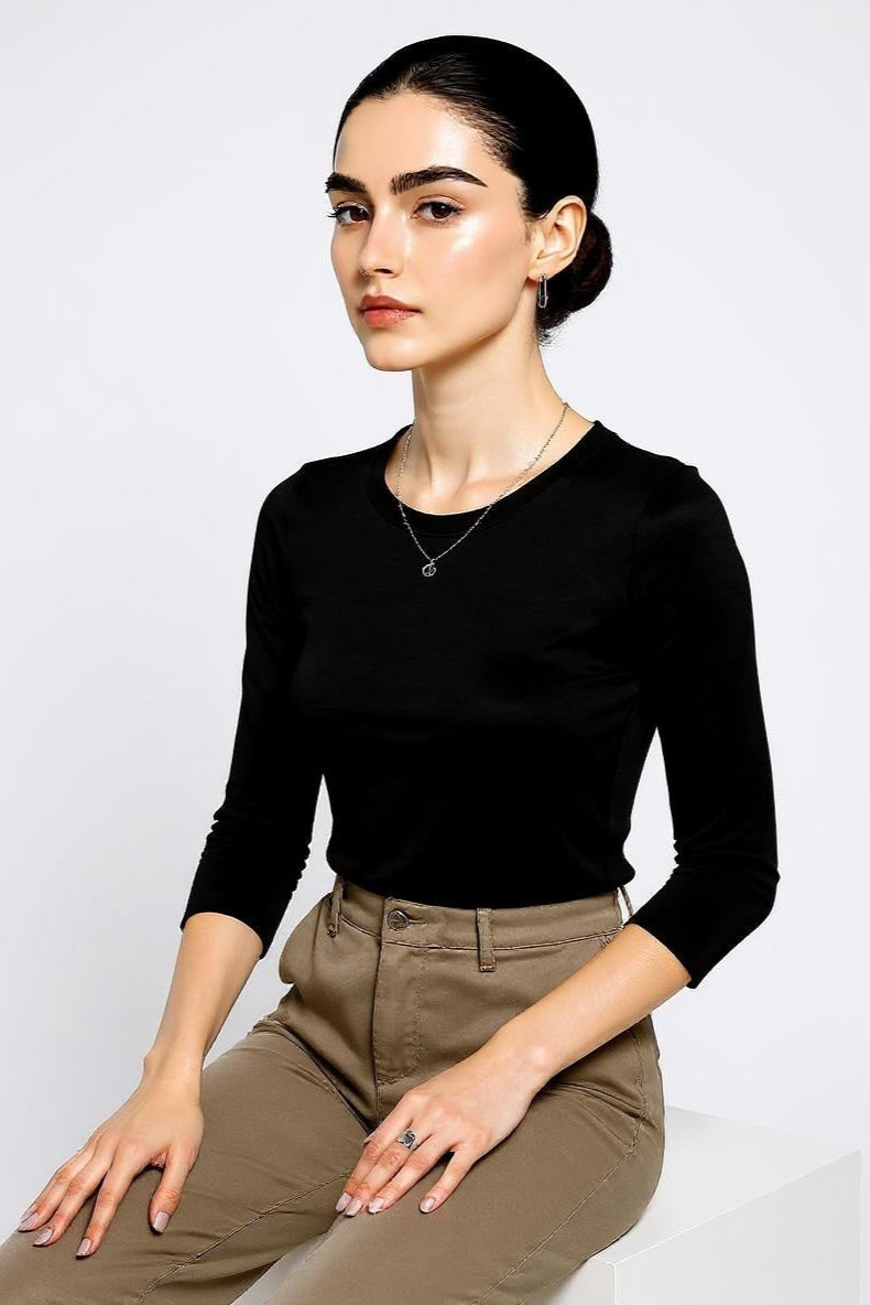 Woman wearing a black long-sleeve top and beige pants against a white background