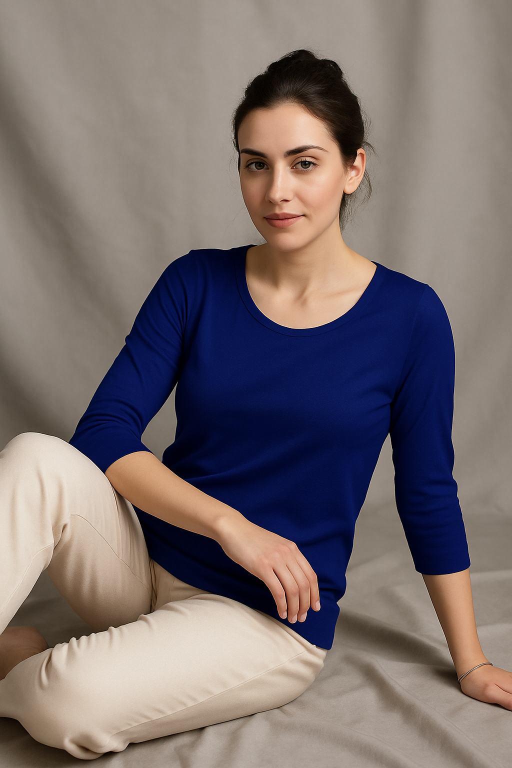 Woman wearing a blue top and white pants sitting on a gray background