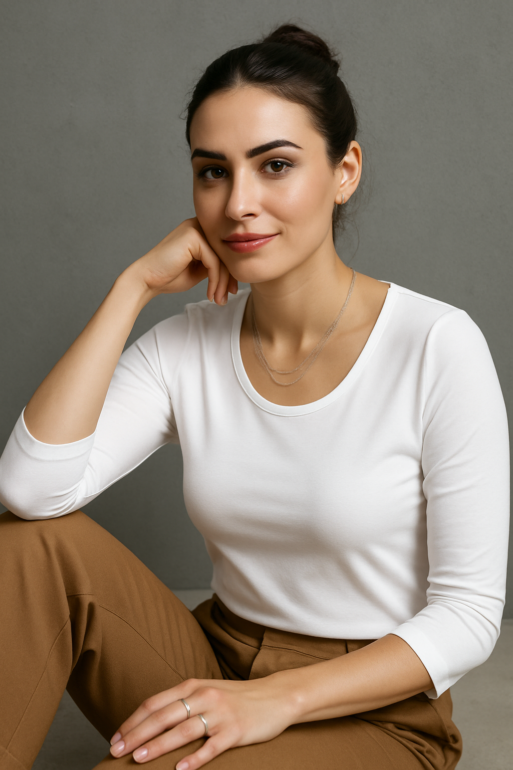 Woman wearing a white long-sleeve top and brown pants against a gray background