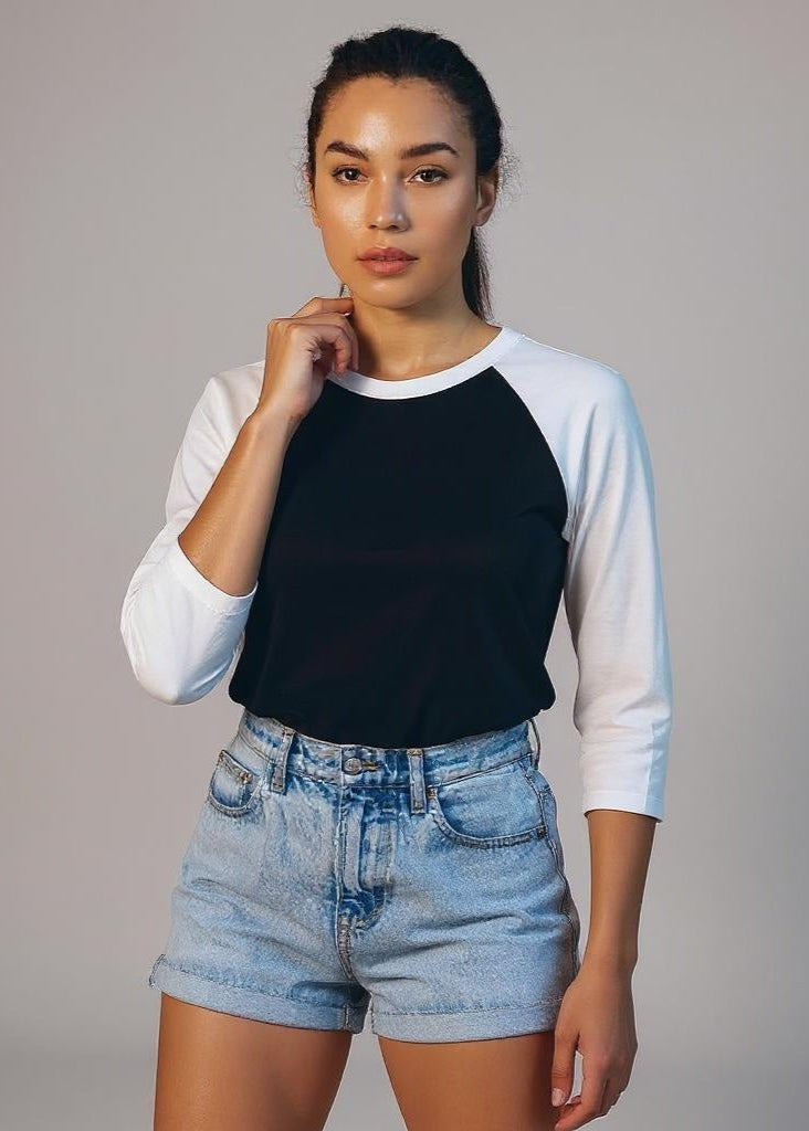 Woman wearing a black and white long-sleeve shirt with denim shorts on a gray background