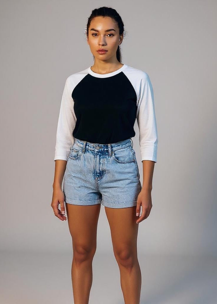 Person wearing a black and white baseball shirt with denim shorts on a gray background