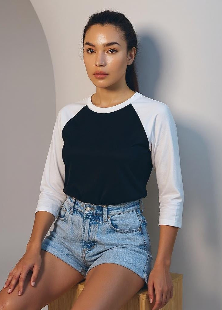Woman wearing a black and white long-sleeve shirt and denim shorts against a plain background