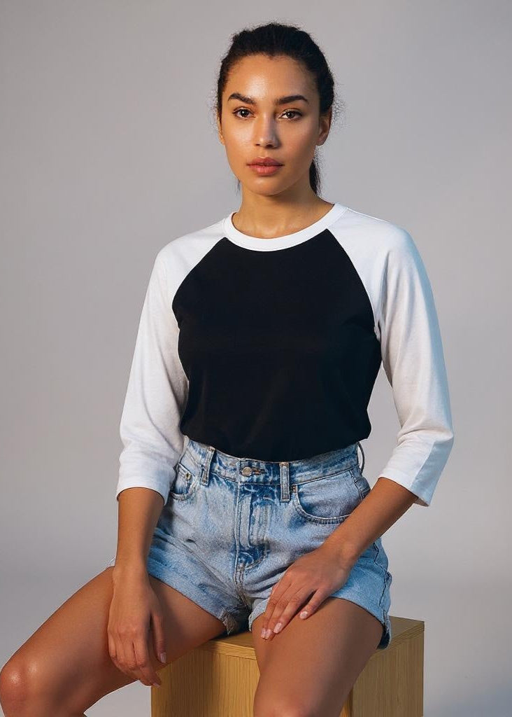 Woman wearing a black and white baseball shirt with denim shorts on a gray background