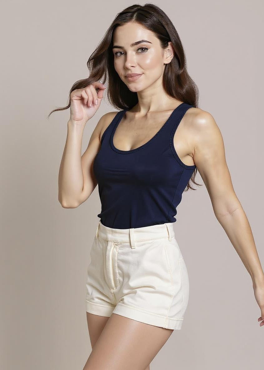 Woman wearing a navy tank top and white shorts against a beige background