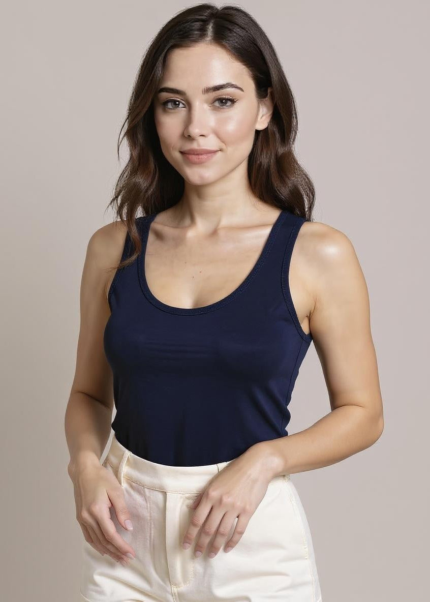 Woman wearing a navy tank top and white pants against a plain background