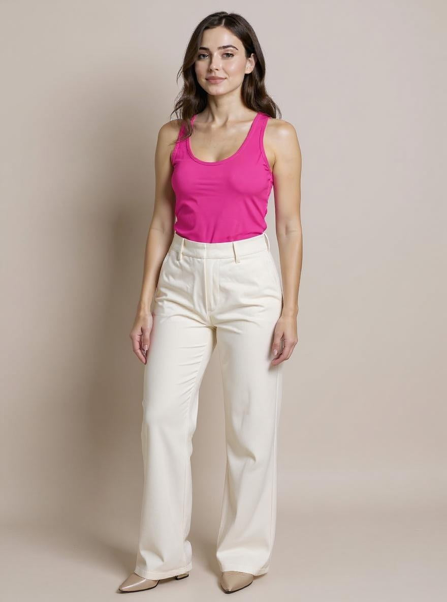 Woman wearing a pink tank top and white pants against a beige background