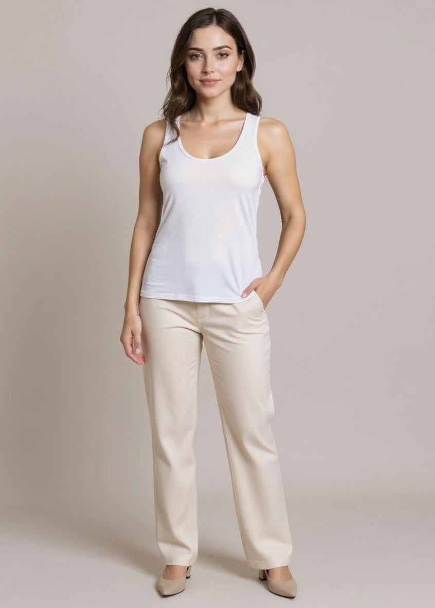 Woman wearing a white tank top and beige pants against a plain background