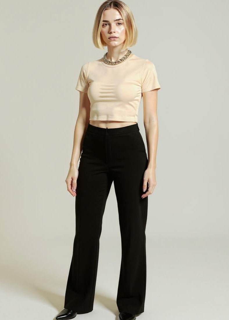 Woman wearing a beige top and black pants against a plain background