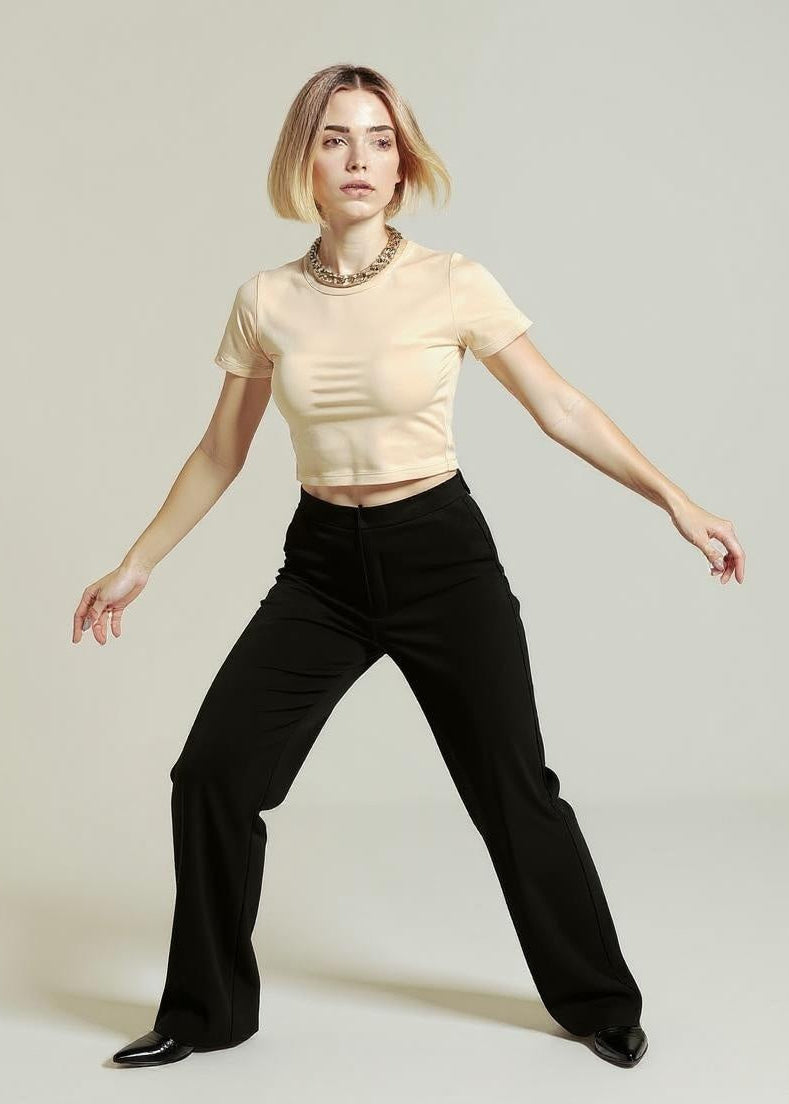 Woman wearing a beige top and black pants on a plain background