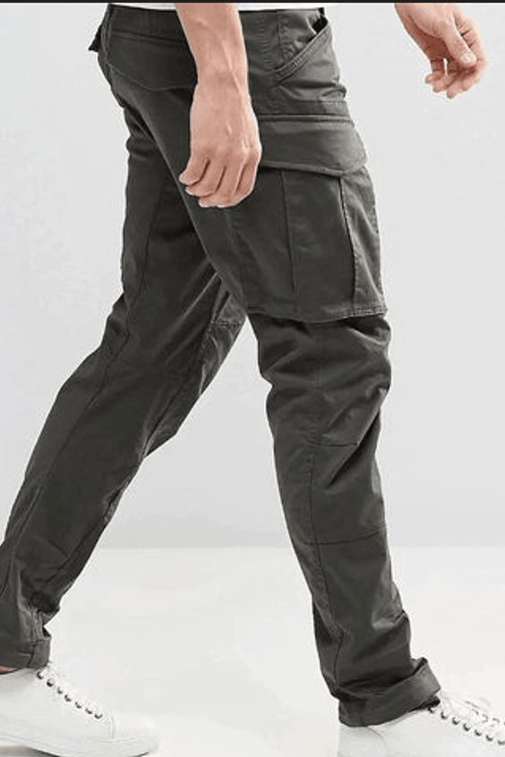 A person standing against a white background, wearing green regular fit cargo pants with multiple pockets and metallic zip detailing.