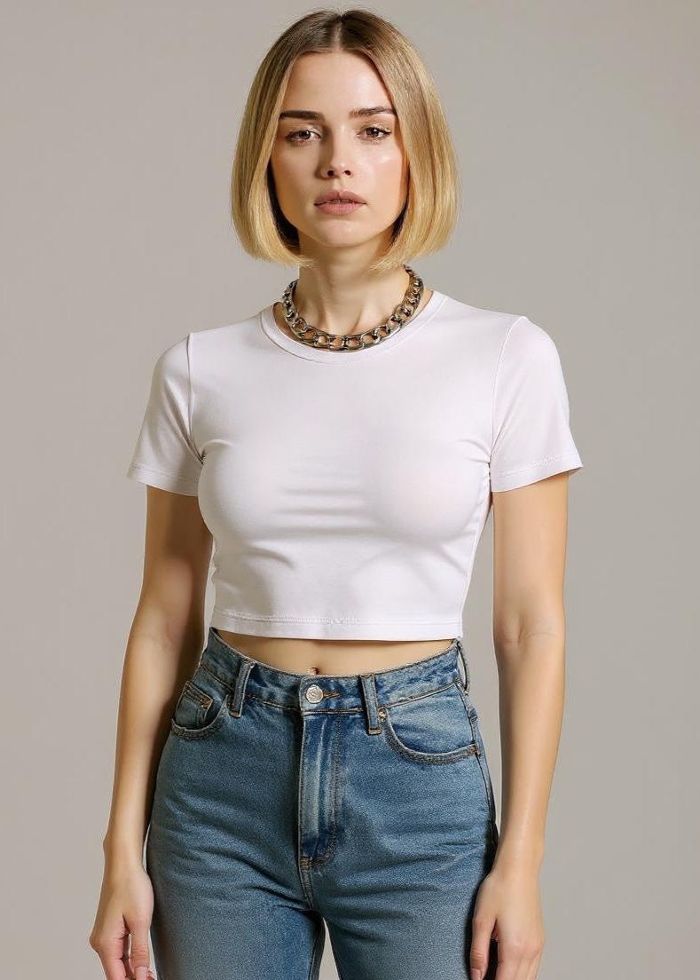 Woman wearing a white crop top and blue jeans against a plain background