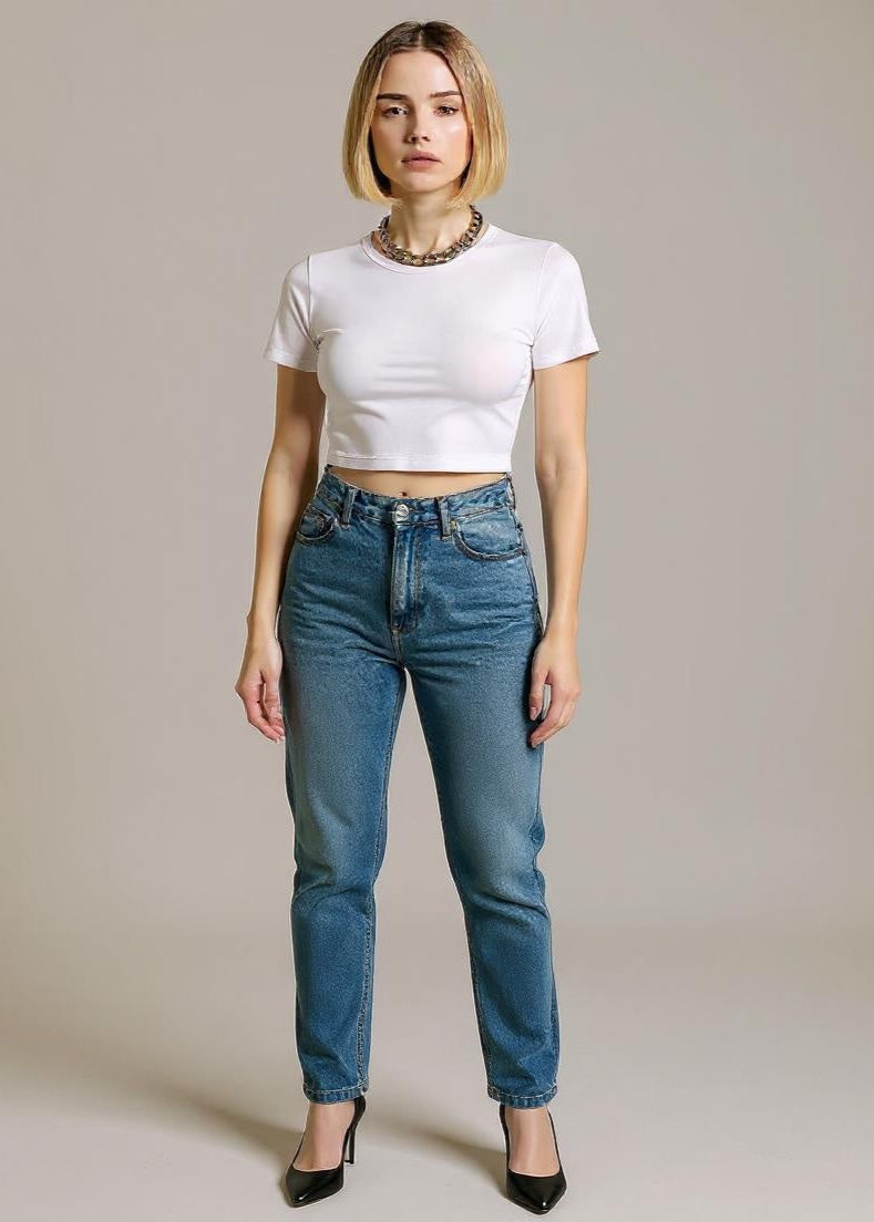 Woman wearing a white crop top and blue jeans against a plain background