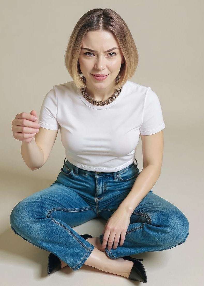 Woman wearing a white t-shirt and blue jeans sitting on a beige background