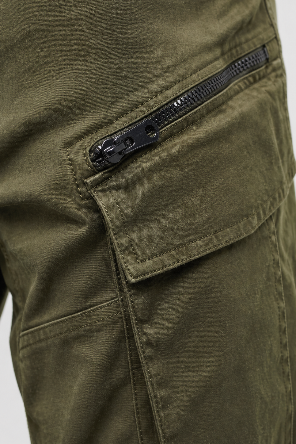 Close-up of olive green cargo pants with a zipper pocket on a light gray background