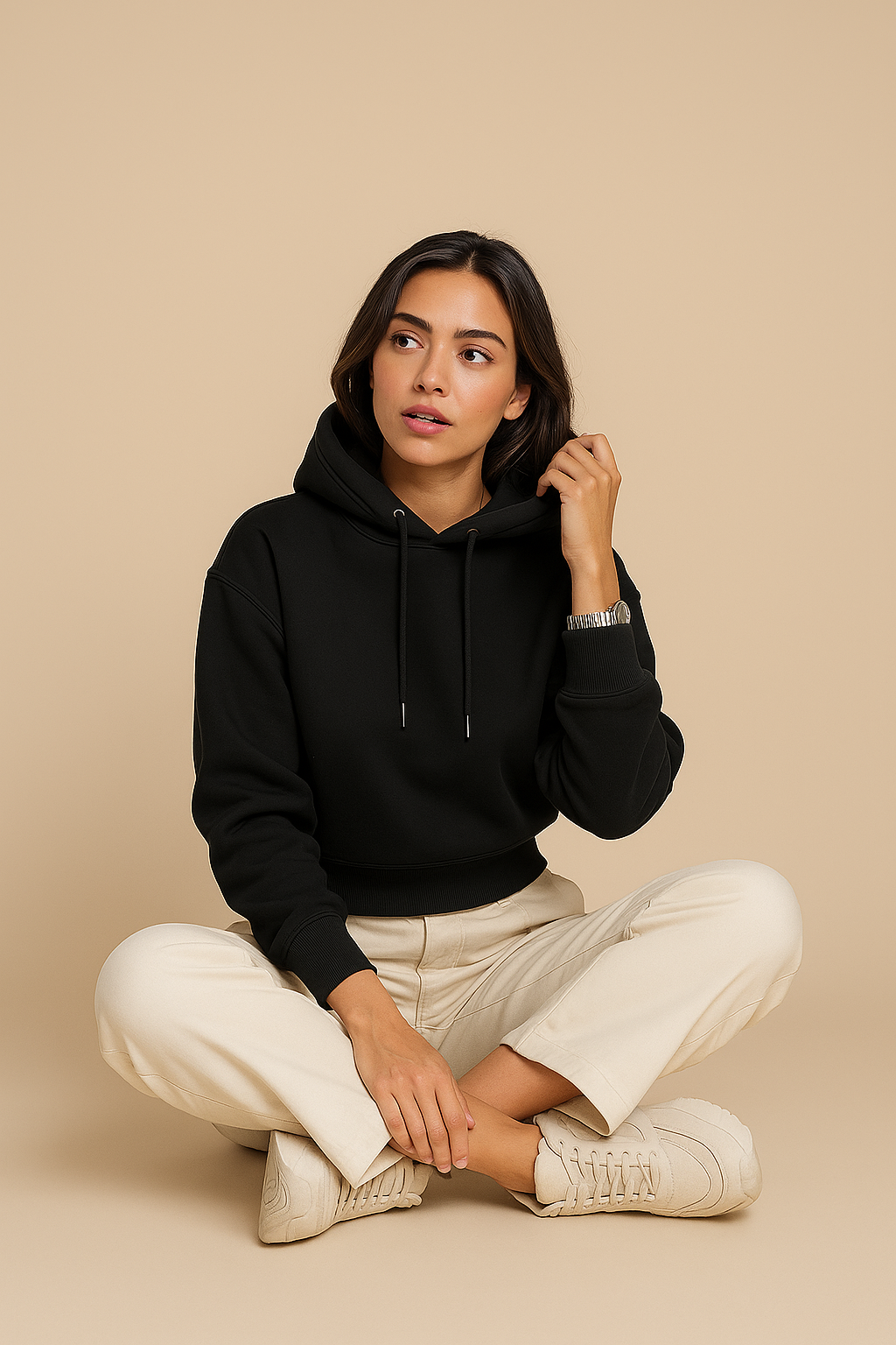 Woman wearing a black hoodie and beige pants sitting on a beige background
