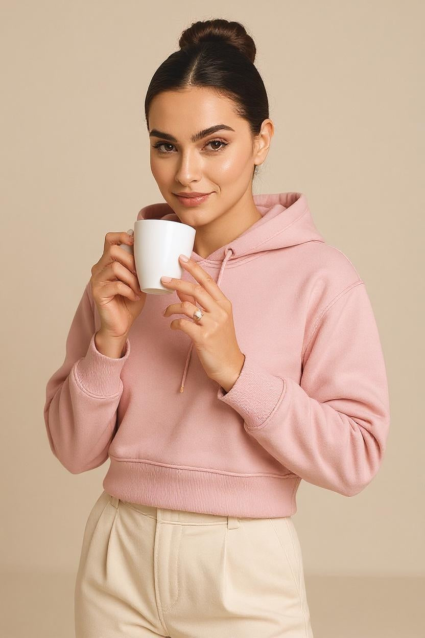 Woman wearing a pink hoodie holding a white mug against a beige background