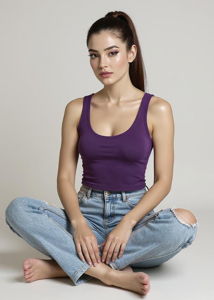 Woman wearing a purple tank top and blue jeans sitting on the floor against a plain background
