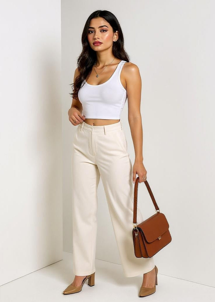 Woman wearing a white tank top and beige pants, holding a brown handbag against a white background