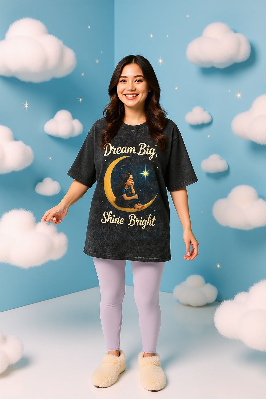 Woman wearing a t-shirt with 'Dream Big, Shine Bright' design in a cloud-themed room.
