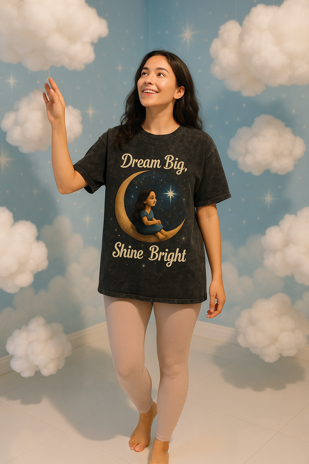 Woman wearing a 'Dream Big, Shine Bright' t-shirt with a celestial design against a cloud-themed background.