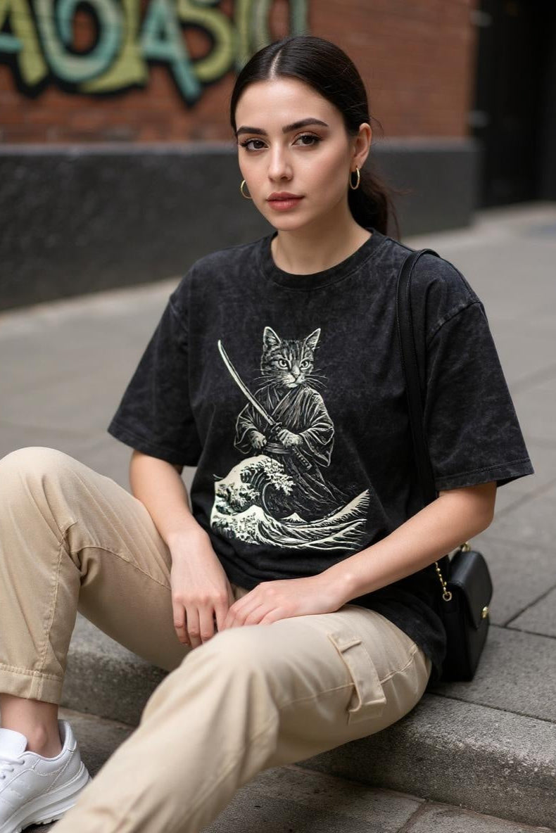 Woman wearing a black t-shirt with a graphic design, sitting on a street.
