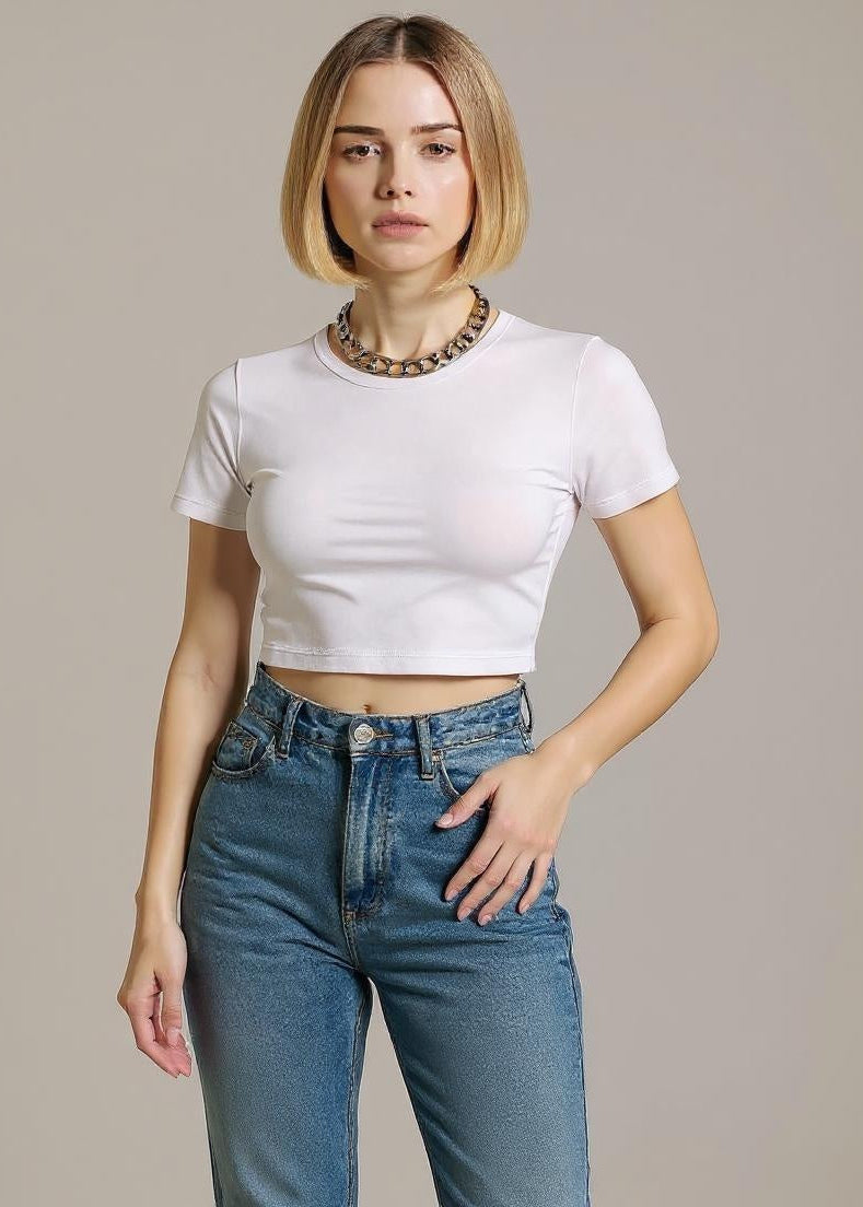 Woman wearing a white crop top and blue jeans against a plain background